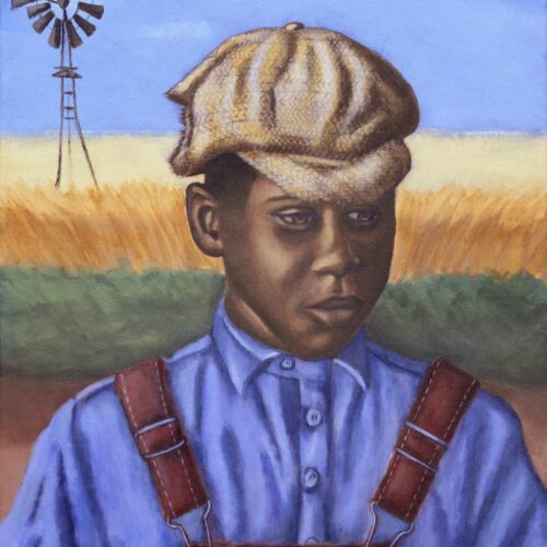 African American boy wearing blue shirt, red overalls, and tattered tan cap. He is standing in front of a field.